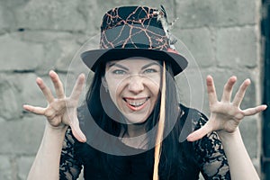 Close-up portrait of woman dressed in a Halloween costume against stone wall. witch with a bright orange lock of hair in a black