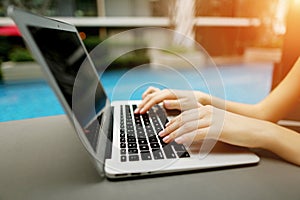 Close up portrait of woman hands pressing keyboard buttons on laptop sunny day swimming pool