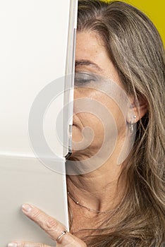 close-up portrait of a woman with her face behind a blank page against yellow background