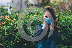 Close-up portrait of woman in protective medical mask on her face, holding hands near the face, surprised outdoor.