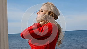 Close up portrait of woman running hand through curly hair blowing in wind by sea on beach. Happy female over blue sky.