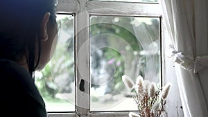 Close up portrait of a woman sat blankly looking at the outside through the glass windows at home. Emotional loneliness concept.