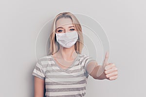 Close up portrait of woman showing thumb up wearing white face mask isolated on grey colored background