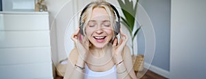 Close up portrait of woman smiling while listening to music in wireless headphones, singing with eyes closed