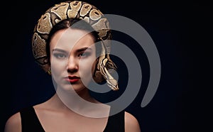 Close up portrait of woman with snake around her head on dark ba