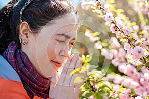 Close-up portrait of a woman sneezing from pollen of flowers. Concept of season allergy