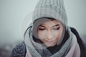 Close up portrait of woman who looking down on misty background. Photo of beautiful fashion model with a cap in winter time. Girl