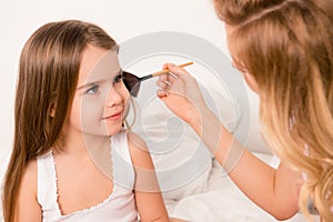 Close up portrait of woman doing maquillage to her cute daughter