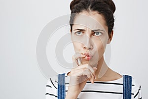 Close-up portrait of worried young european female, frowning and folding lips while thinking about something, looking up