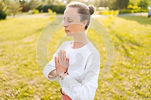 Close-up portrait of yogini female with emotion of serenity and tranquility performing Namaste gesture on nature, closed
