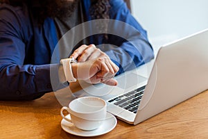 Close up portrait of young adult man freelancer in casual style sitting in cafe with laptop and cup of coffee, looking to the