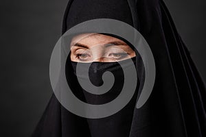 Close up portrait of young, adult woman in black burqa  with hidden face, isolated on black background