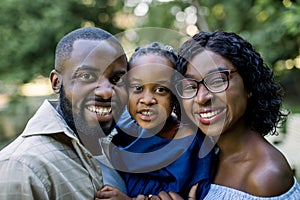 Close up portrait of young African American family with little cute daughter in the summer park. Smiling family looking