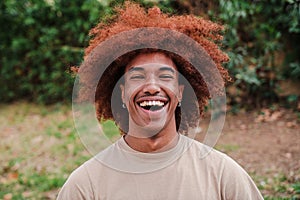 Close up portrait of young african american toothy man with afro hair smiling looking at camera outdoors. Head shot of a