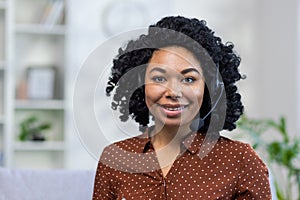 Close-up portrait of a young African-American woman sitting cross-legged on the couch wearing a headset and smiling at