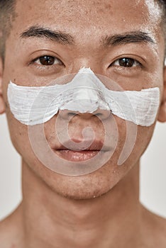 Close up portrait of young asian man with problematic skin and hyperpigmentation applied mask on his face, looking at photo