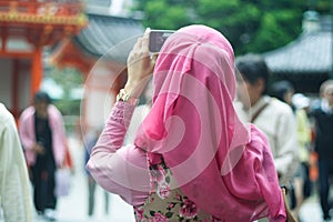 Close up portrait of young Asian muslim woman wearing pink hijab holding and looking at smartphone taking picture