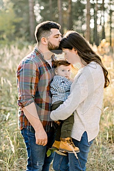 Close up portrait of young attractive family with little baby son, posing in beautiful autumn pine forest at sunny day