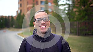 Close up portrait of young attractive man in the glasses looking to the camera and smiling on the city background