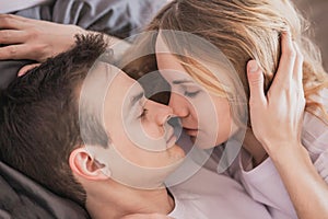 Close up portrait of young attractive romantic couple hugging and kissing, laying down on a bed, being loving with each other.