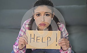 Close up portrait of young attractive and sad hispanic woman sitting at home couch looking stressed and worried showing help sign