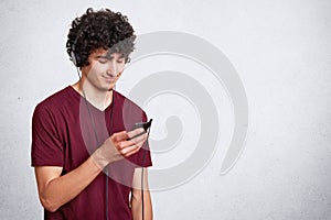 Close up portrait of young attractive teenager with dark crisp hair. Guy listens to music or watches video from his smart phone.