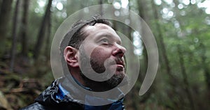 Close-up portrait of a young bearded man sitting in nature between forest