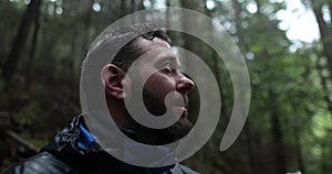 Close-up portrait of a young bearded man sitting in nature between forest