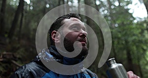 Close-up portrait of a young bearded man sitting in nature between forest