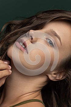 Close-up portrait of young beautiful adorable girl looking at camera isolated over dark green studio background. Natural