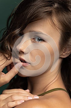 Close-up portrait of young beautiful adorable girl looking at camera isolated over dark green studio background. Natural