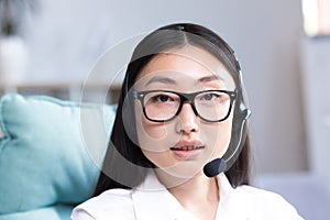 Close-up portrait of a young beautiful asian woman with glasses smiling and looking at the camera, uses a headset for