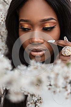 Close-up portrait of a young beautiful black woman with clean skin and manicure near flowers on the street. Healthy and beauty