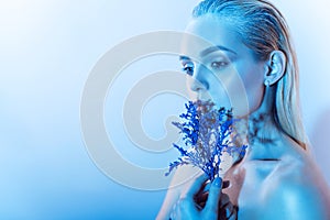 Close up portrait of young beautiful blond model with nude make up, slicked back hair holding a branch of blue flowers photo