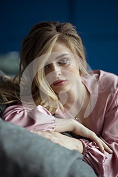 Close-up portrait of young beautiful blonde woman with wavy hair in a pink peignoir with a plunging neckline