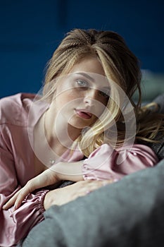 Close-up portrait of young beautiful blonde woman with wavy hair in a pink peignoir with a plunging neckline