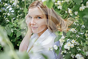 Close up of a portrait of a young beautiful blonde woman in a white shirt with jasmine flowers. Romantic atmosphere and dreamy