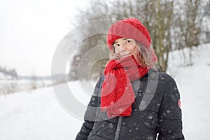 Close-up portrait of young beautiful caucasian woman with pink hair wearing red hat and scarf during snowfall on winter day