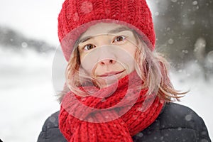 Close-up portrait of young beautiful caucasian woman with pink hair wearing red hat and scarf during snowfall on winter day