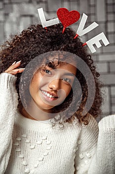 Close-up portrait of a young beautiful curly-haired girl with a rim with the inscription love on her head. the girl posing and