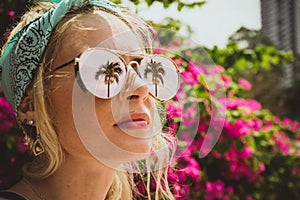 Close-up portrait of a young beautiful girl in glasses with reflection of tropical palms. Summer rest. Modern tourist