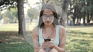 Close Up Portrait of Young Beautiful Girl Sitting On Lawn In Park Using Phone, On-line Shopping Concept