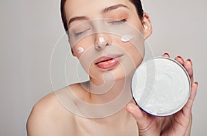 Close-up portrait of a young beautiful half-naked girl with closed eyes holds face cream in her left hand