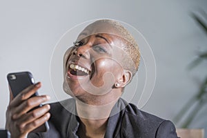 Close up portrait of young beautiful and happy trendy black afro american woman holding and using mobile phone isolated on grey ba