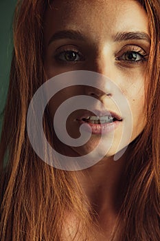 Close-up portrait of young beautiful red-headed woman without makeup isolated over dark green studio background. Natural