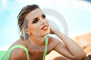 Close-up portrait of young beautiful sexy tanned slim blonde woman with wet hair in green wet swimming suit near swimming pool
