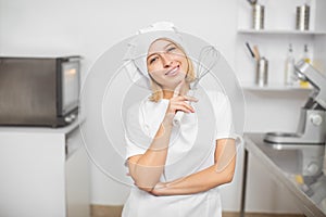 Close up portrait of young beautiful smiling blond girl, professional pastry chef, wearing white uniform, apron and chef