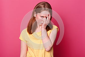 Close of up portrait of young beautiful student female, covers face with hand, being tired after school, has lots of homework,