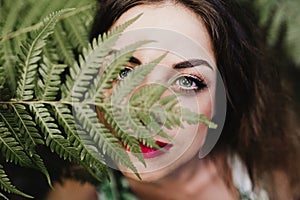 close up portrait of a young beautiful woman among green fern leaves looking at the camera. Beauty concept