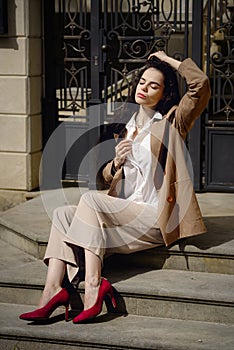 Close up portrait of young beautiful woman with long brunette curly hair posing against building background. sitting on